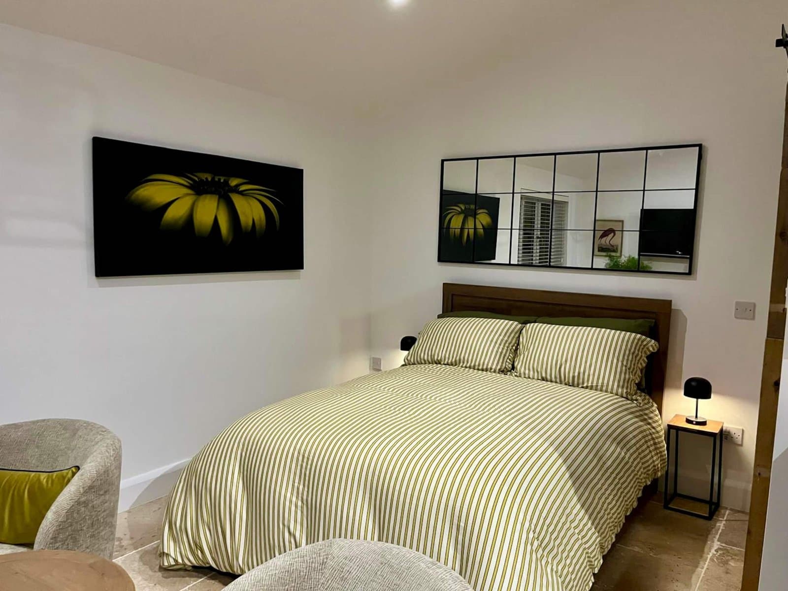 The double bed made up in green striped linen, under a large sunflower print